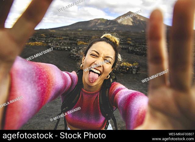 Happy woman sticking out tongue and taking selfie with landscape in background