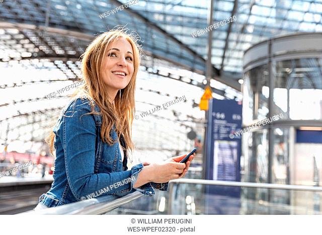 Smiling woman with smartphone at the train station, Berlin, Germany