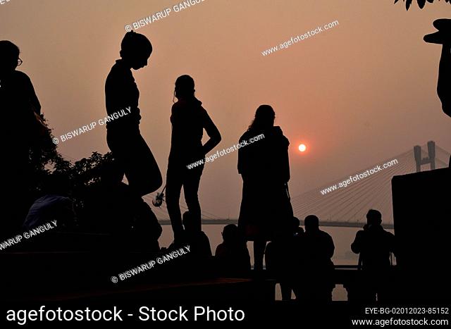 Dec 31, 2022, Kolkata, India. Persons enjoy the sunset across the  Howrah Bridge (Vidyasagar Setu) On River Ganges. scenic beauty of the setting sun on the last...