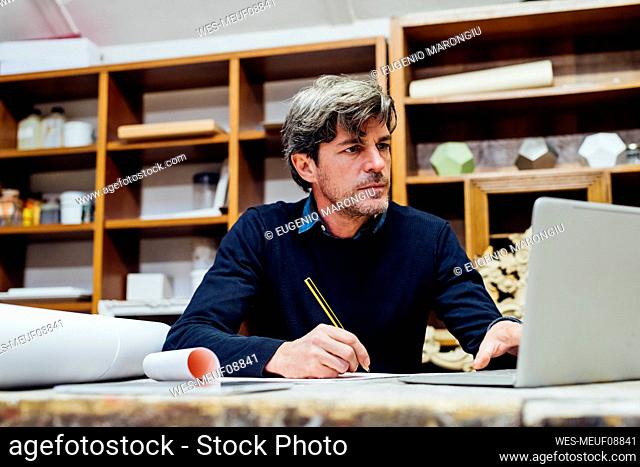 Mature man sketching in front of laptop at workshop