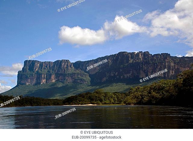 A big Tepui mountain by the coast of a river shoot on a bright day with blue sky and white clouds