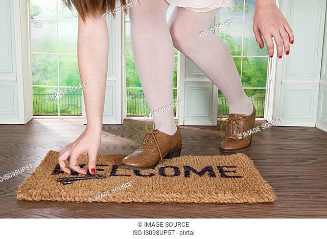 Woman picking up key on welcome mat in small room