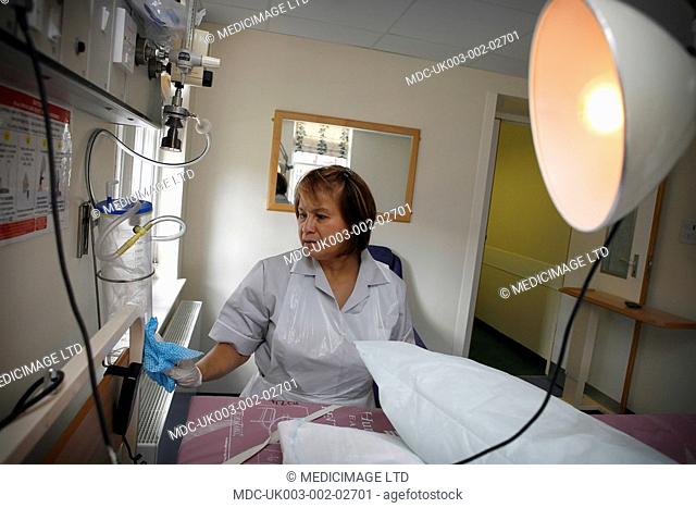 A hospital cleaner cleaning and disinfecting patinet's bed and medical equipment