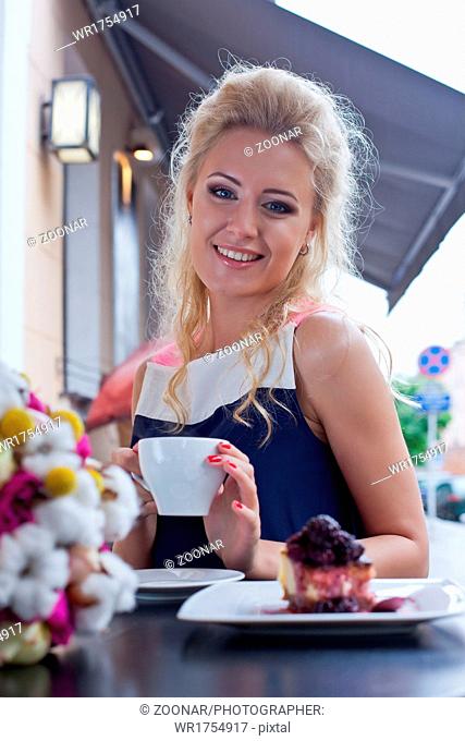 a beautiful young blond girl in summer dress at the table in pavement cafe