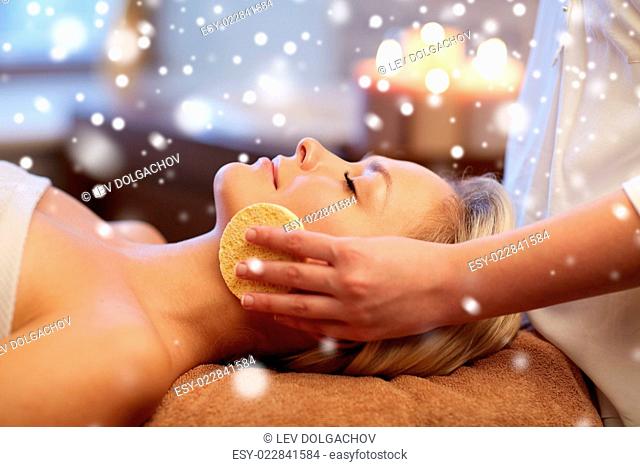people, beauty, spa, skin care and relaxation concept - close up of beautiful young woman lying with closed eyes and having face massage with sponge in spa with...