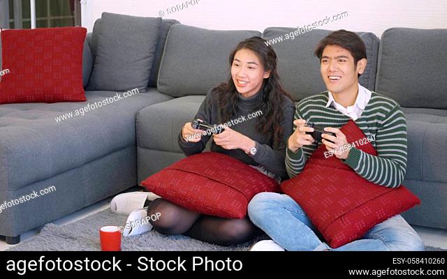 Happy Asian beautiful young family couple husband and wife smile and laugh enjoying funny with each other playing video game, holding joysticks console