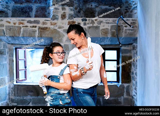Mother and daughter with paintbrush and paint roller facing each other