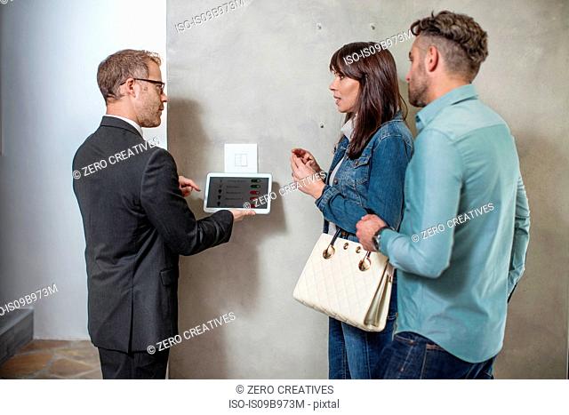 Estate agent standing with couple, using digital tablet to demonstrate technology in new home