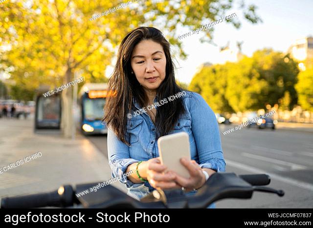 Mature woman renting bicycle through smart phone on footpath