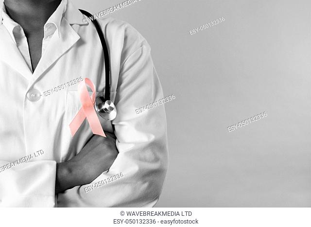 arms crossed nurse wearing breast cancer awareness pink ribbon on a pink background. Close up on the pink ribbon