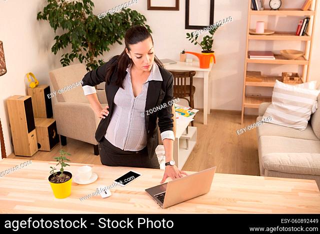 Top view of young pregnant business woman typing on laptop computer while working at home. Brunette lady expecting baby