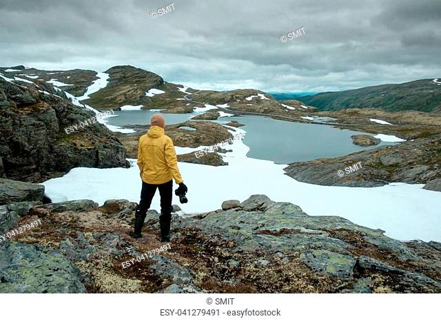 Photographer taking photo of typical norwegian landscape with snowy mountains and clear lake near the famous Aurlandsvegen mountain road, Aurland, Norway