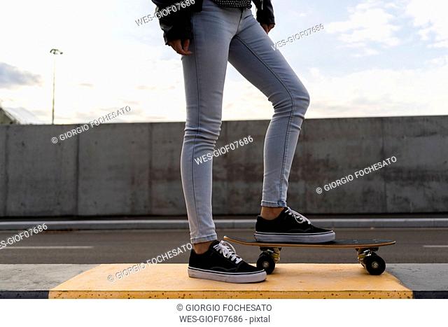Legs of woman with skateboard standing on bollard