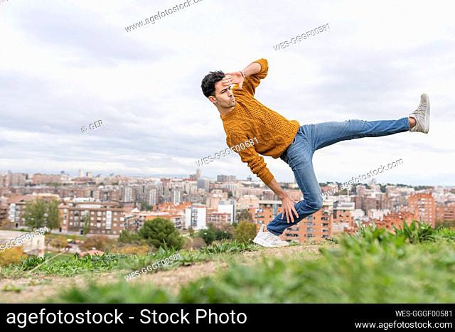 Man doing acrobatic activity on hill in city against cloudy sky