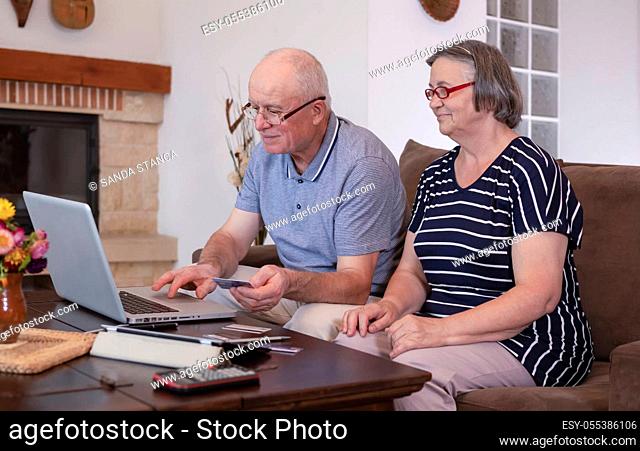 Senior couple shopping online on laptop using credit card at home. Internet banking at home concept. Focus on senior man face