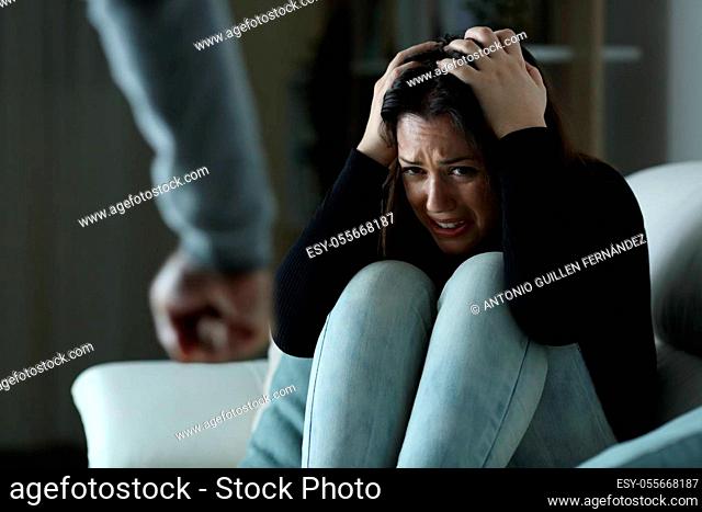 Scared woman victim of gender violence sitting on a couch in the night at home