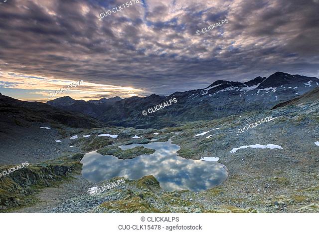 Clouds at dawn are reflected in Lai Ghiacciato framed by peaks, Val Ursaregls, Chiavenna Valley, Valtellina, Lombardy, Italy, Europe
