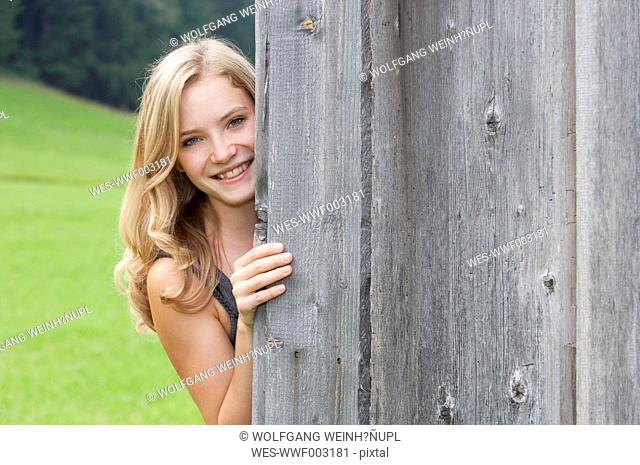 Austria, Salzkammergut, Mondsee, portrait of young woman peeking around a corner