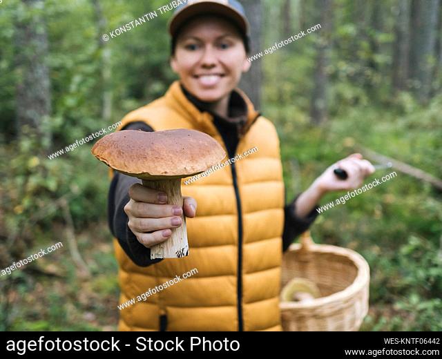 Smiling woman holding mushroom in forest