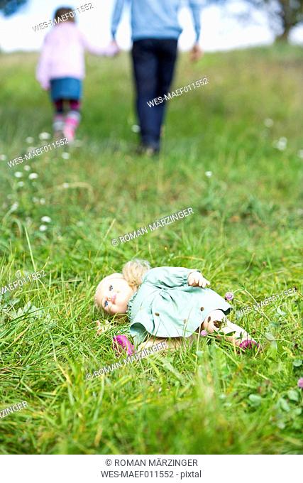 Doll lying on meadow while man going away with little girl