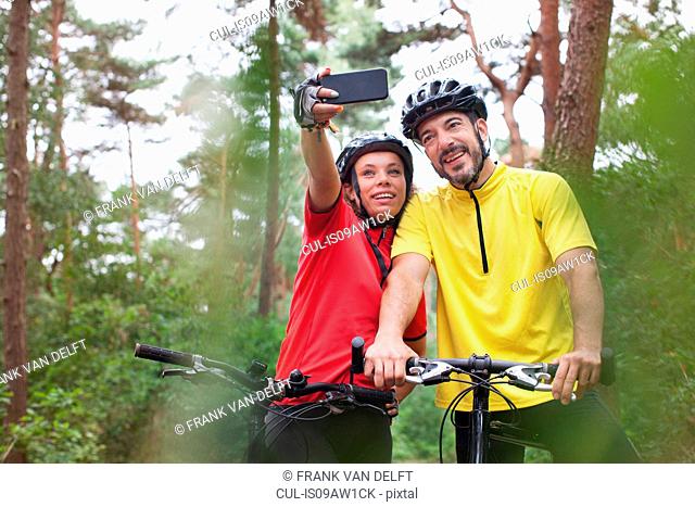 Happy mountain biking couple posing for smartphone selfie in forest
