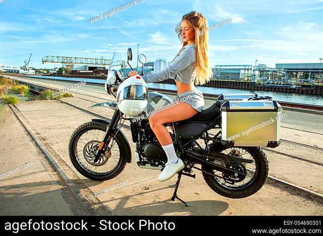 An attractive sexy girl on a motorbike posing outside