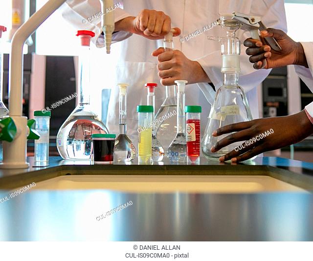 Young male and female scientists preparing experiment with sample bottles in laboratory, cropped