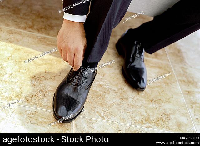 Groom tying the laces of his black shoes on stoneware floor