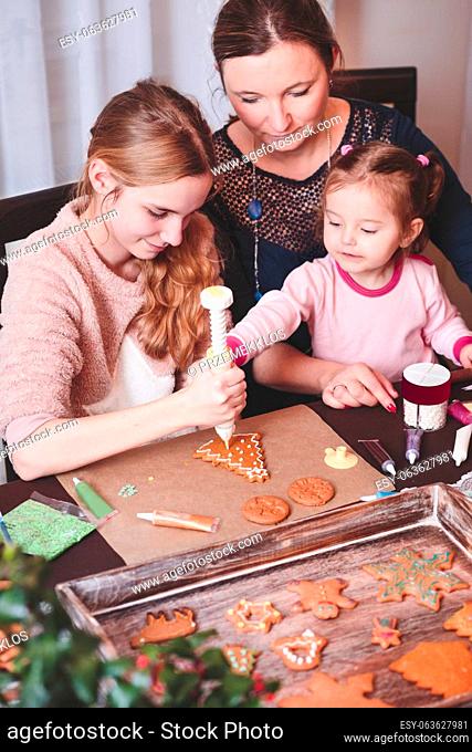 Family decorating baked Christmas gingerbread cookies with frosting