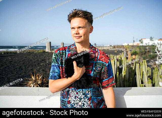 Smiling young man standing with black dog on sunny day