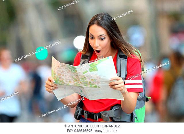 Surprised teen tourist reading a paper guide walking on the street