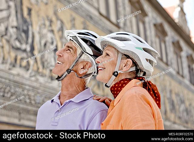 Smiling senior couple wearing cycling helmet looking away while standing at Dresden, Germany
