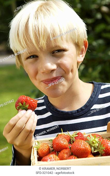 Blond boy with strawberries, one with a bite taken