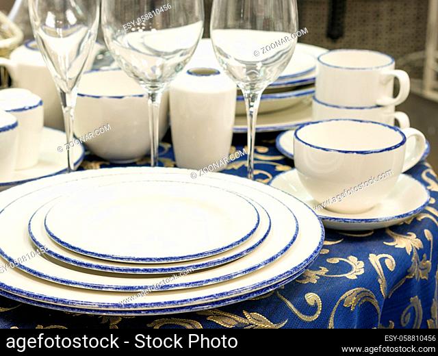 Set of dishes close up on table with blue tablecloth. Stack of plates, wine glasses and cups on restaurant table. Shallow DOF