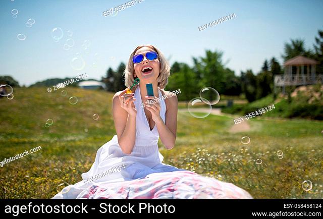 Young beautiful woman outdoors. Happy pretty blond girl, smiling playing with bubble blower