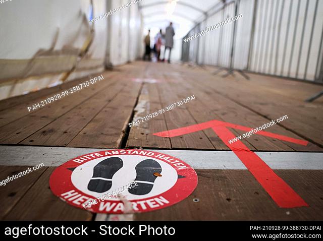 27 September 2021, Hamburg: An arrow and a sticker with the text ""Please keep your distance - Wait here"" can be seen in the entrance area to a test centre for...