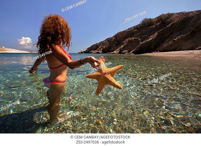 Woman in the sea with a starfish in her hand at Agios Georgios beach, Folegandros, Cyclades Islands, Greek Islands; Greece, Europe