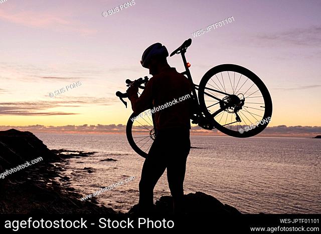Cyclist carrying bicycle in front of sea at sunrise