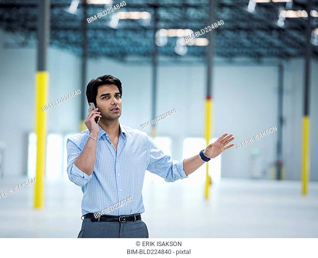 Indian businessman talking on cell phone in empty warehouse