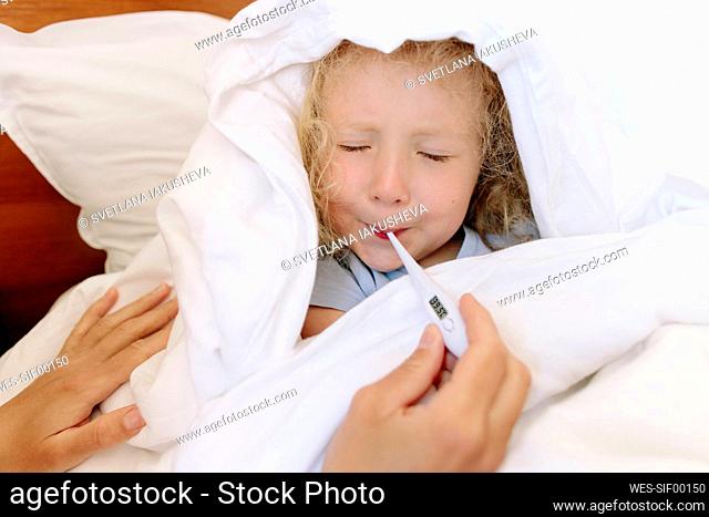 Sick daughter avoiding to use thermometer by mother in bedroom