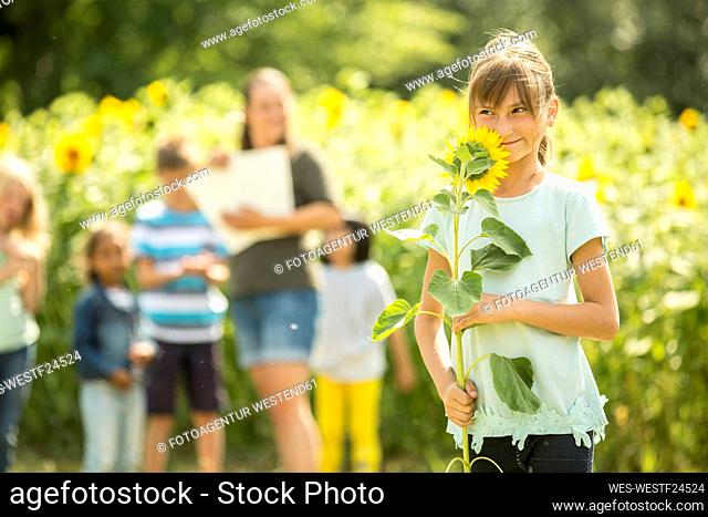 Little girl holding sunflower, teacher and friends standing in background