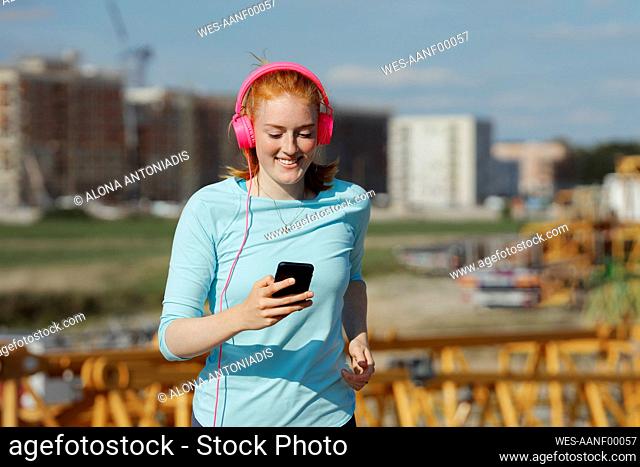 Woman with headphones using mobile phone while jogging on sunny day