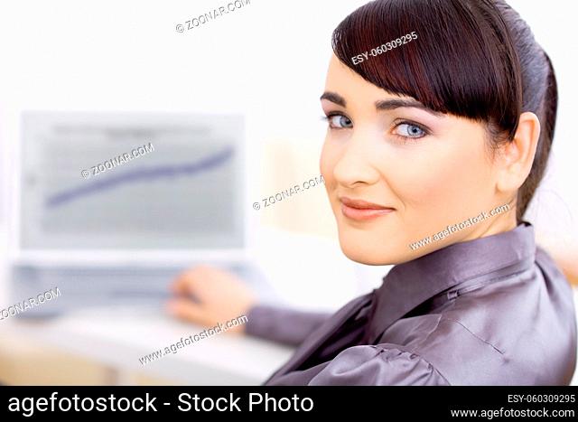 Happy smiling businesswoman working at her desk, looking back at camera