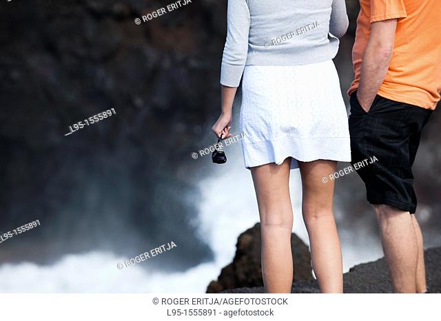 Couple of tourists at Los Hervideros the Boiling ones, natural tourist attraction on the coast where solidified volcano lava flows have been eroded by the...