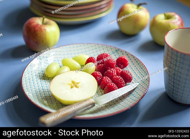Apple, grapes and raspberries with a knife on a ceramic plate