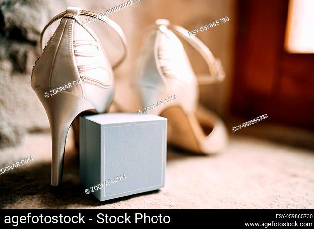 Close-up of a ring box with white bride's shoes in a room with shallow depth of field. High quality photo