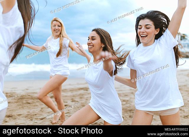 Carefree female friends with arms outstretched enjoying at beach during vacations