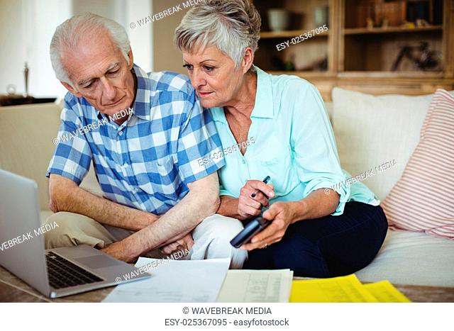 Worried senior couple checking bills in living room