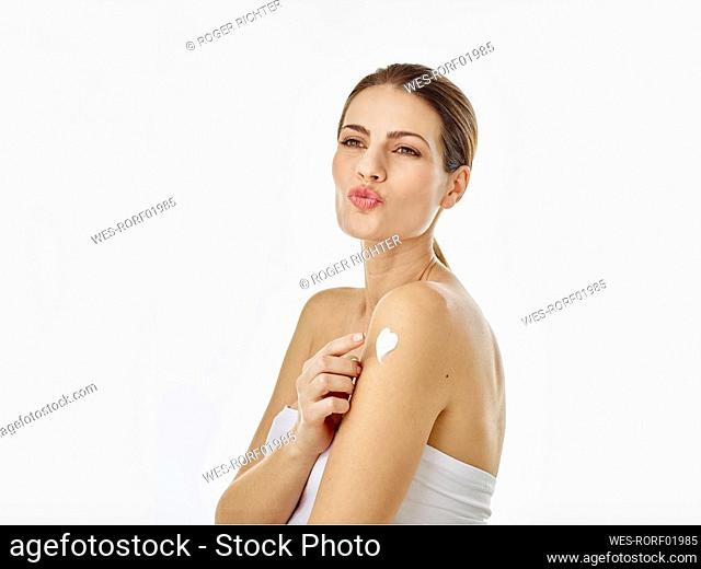 Portrait of woman pouting mouth applying body cream on her arm