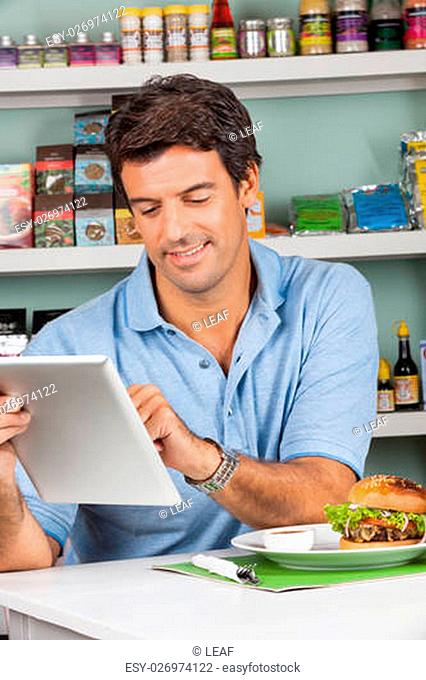 Portrait of mid adult male customer with snacks at table using digital tablet in grocery store
